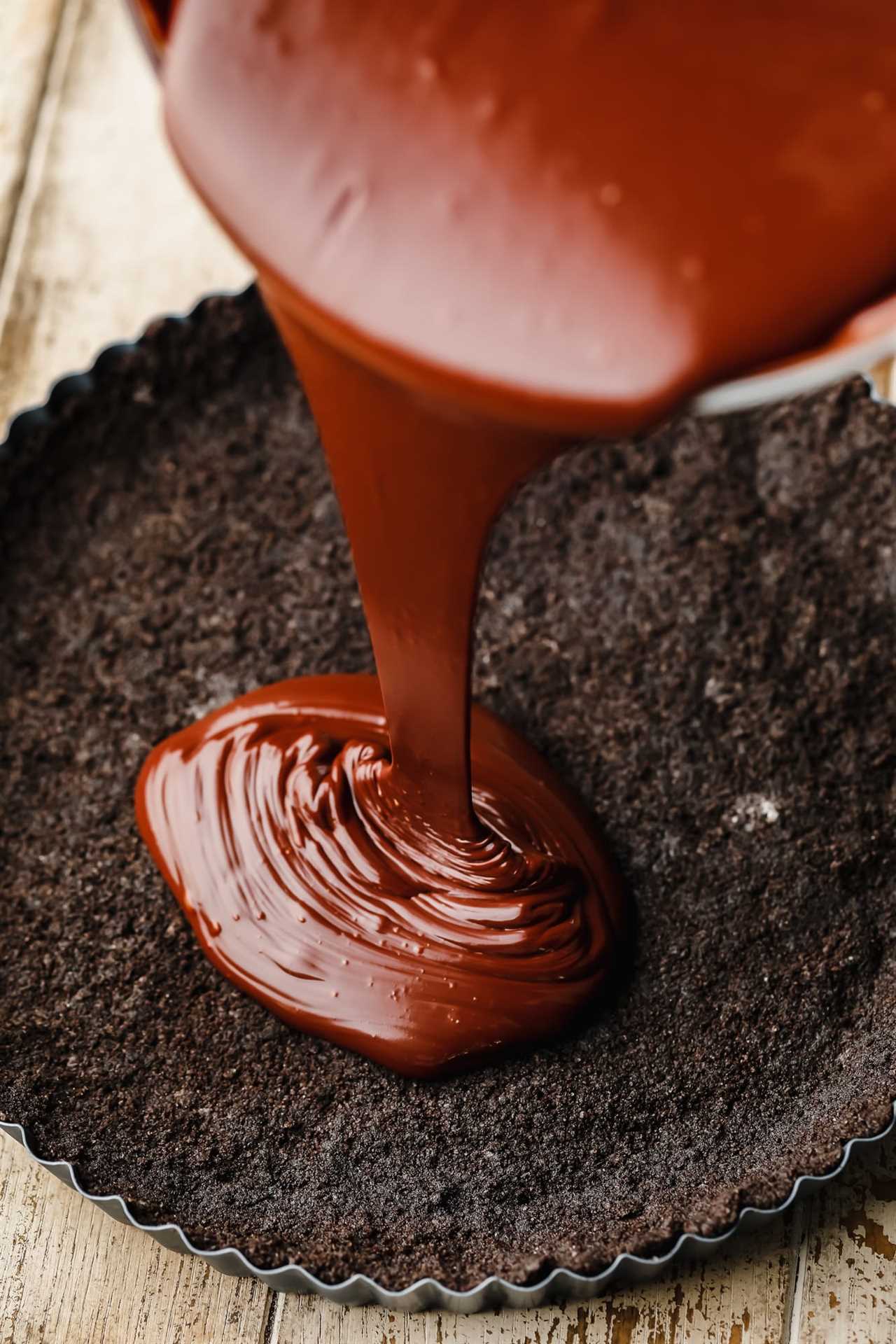 pouring chocolate ganache into an oreo cookie crust in a tart pan.