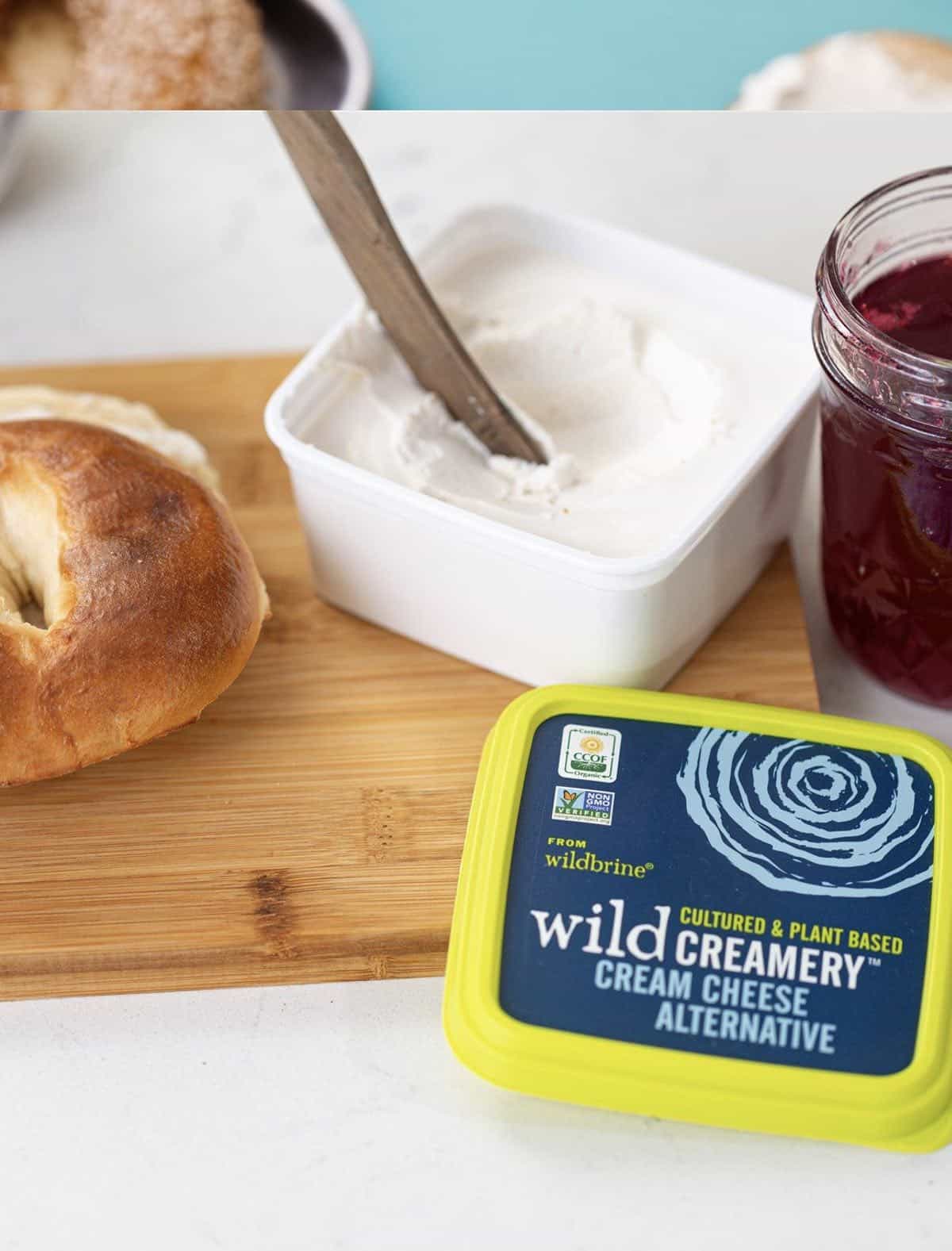 wild creamery tub of dairy free cream cheese with a knife and jam on a cutting board. 