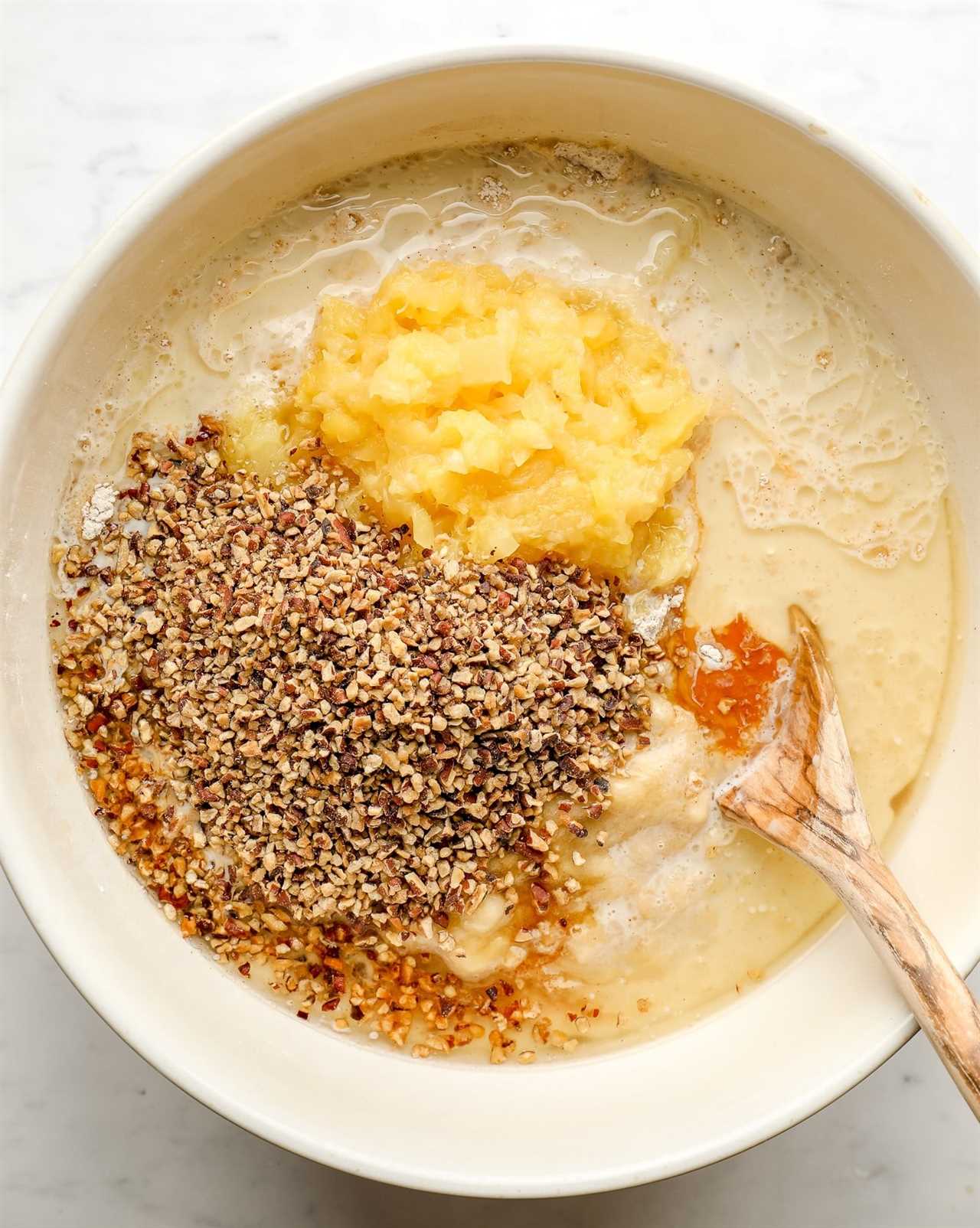 using a wooden spoon to stir hummingbird cake ingredients together in a large white bowl.