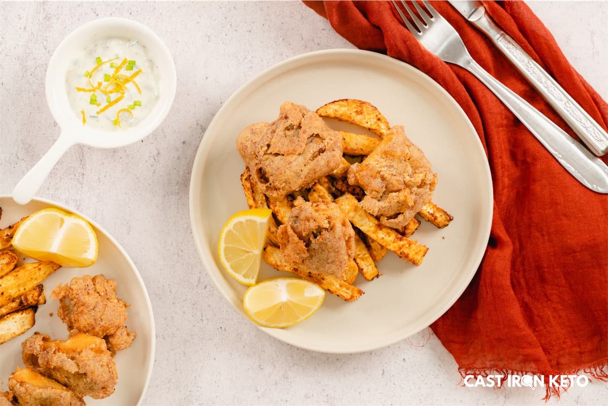 a white plate topped with keto-friendly fish and chips next to a bowl of lemon wedges.