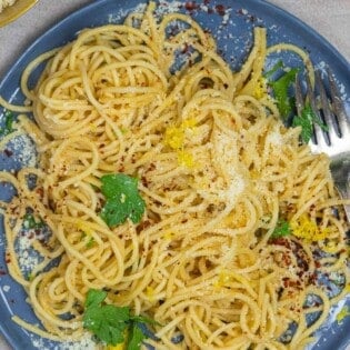 lemon pasta on a plate with a garnish of fresh parsley and a sprinkle of parmesan cheese, red pepper flakes, and lemon zest.