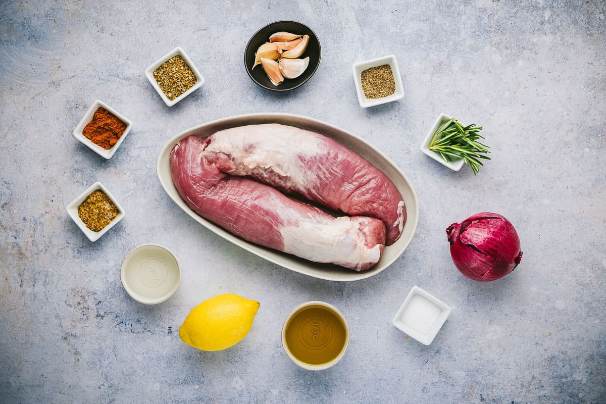 Ingredients for pork Souvlaki, including garlic, pork tenderloin, lemon, rosemary, white wine vinegar, oregano, Dijon, pepper, salt, and oil.