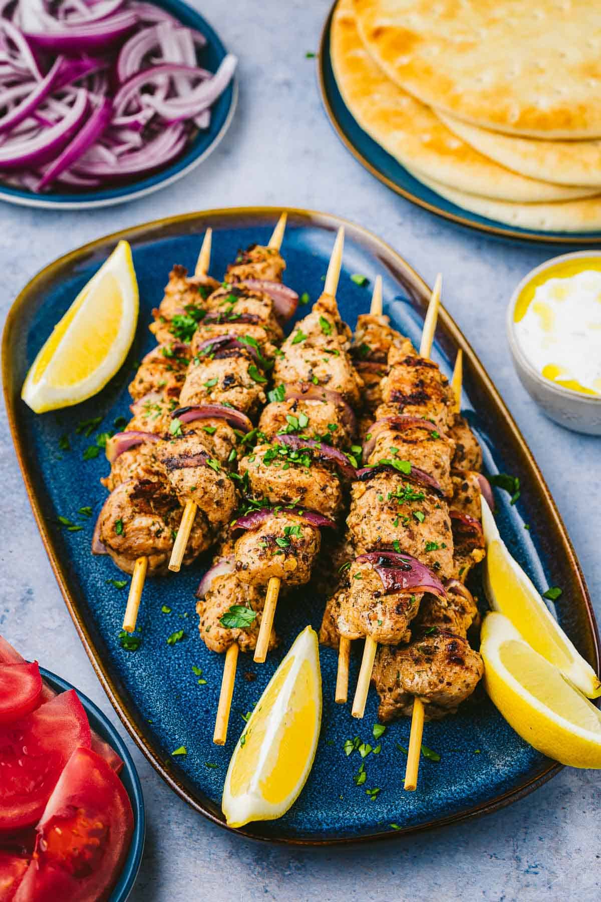 Pork souvlaki skewers on a serving platter with lemon wedges on the side.