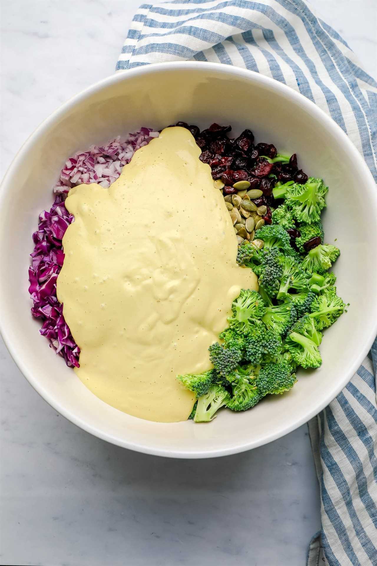 the ingredients for vegan broccoli salad with yellow creamy dressing poured on top in a large white bowl.