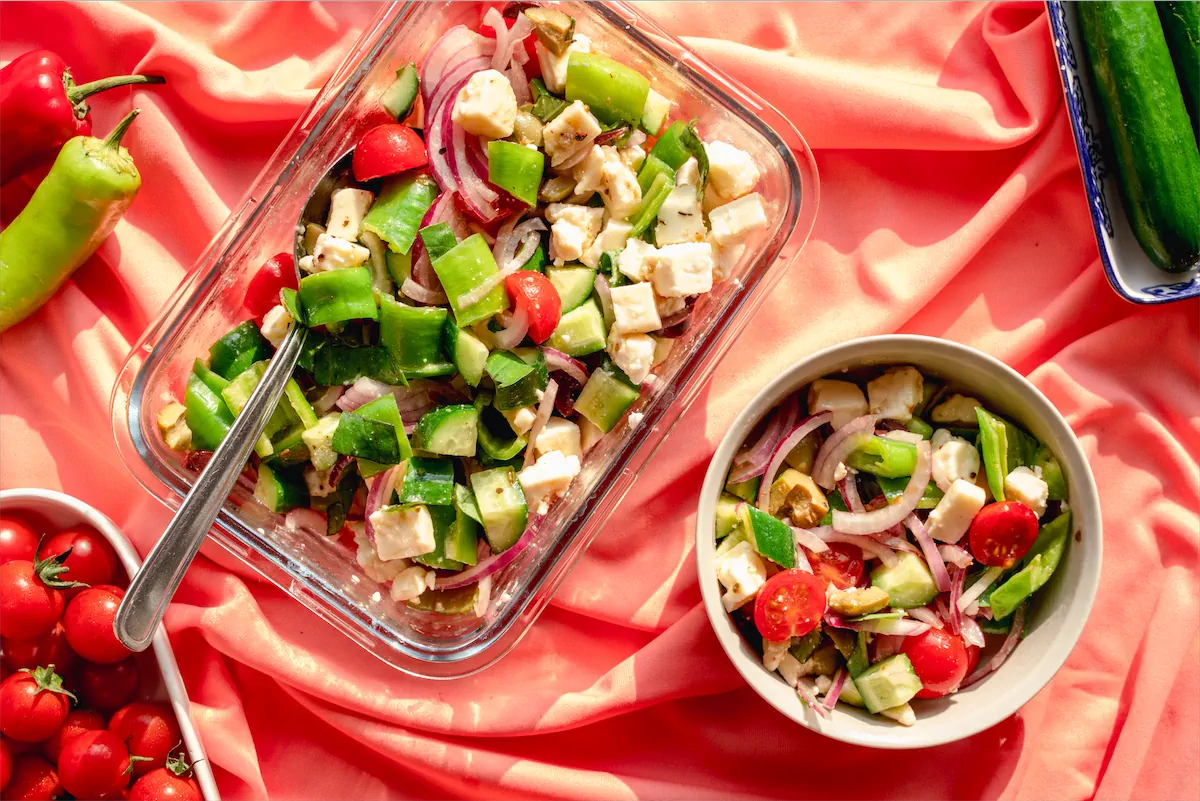 A bowl of keto salad recipe served from a glass dish full of salad next to it.