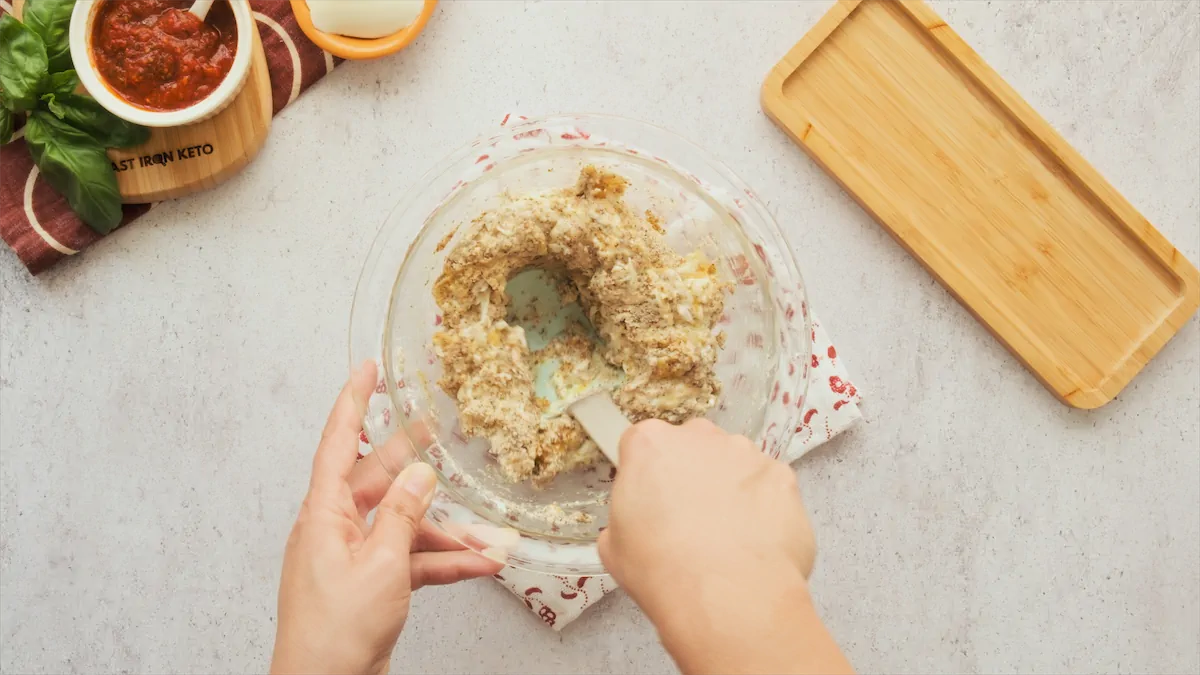 Almond meal, egg, salt, baking powder, mixed dried herbs, cheese, being stirred in a bowl with a silicone spatula.