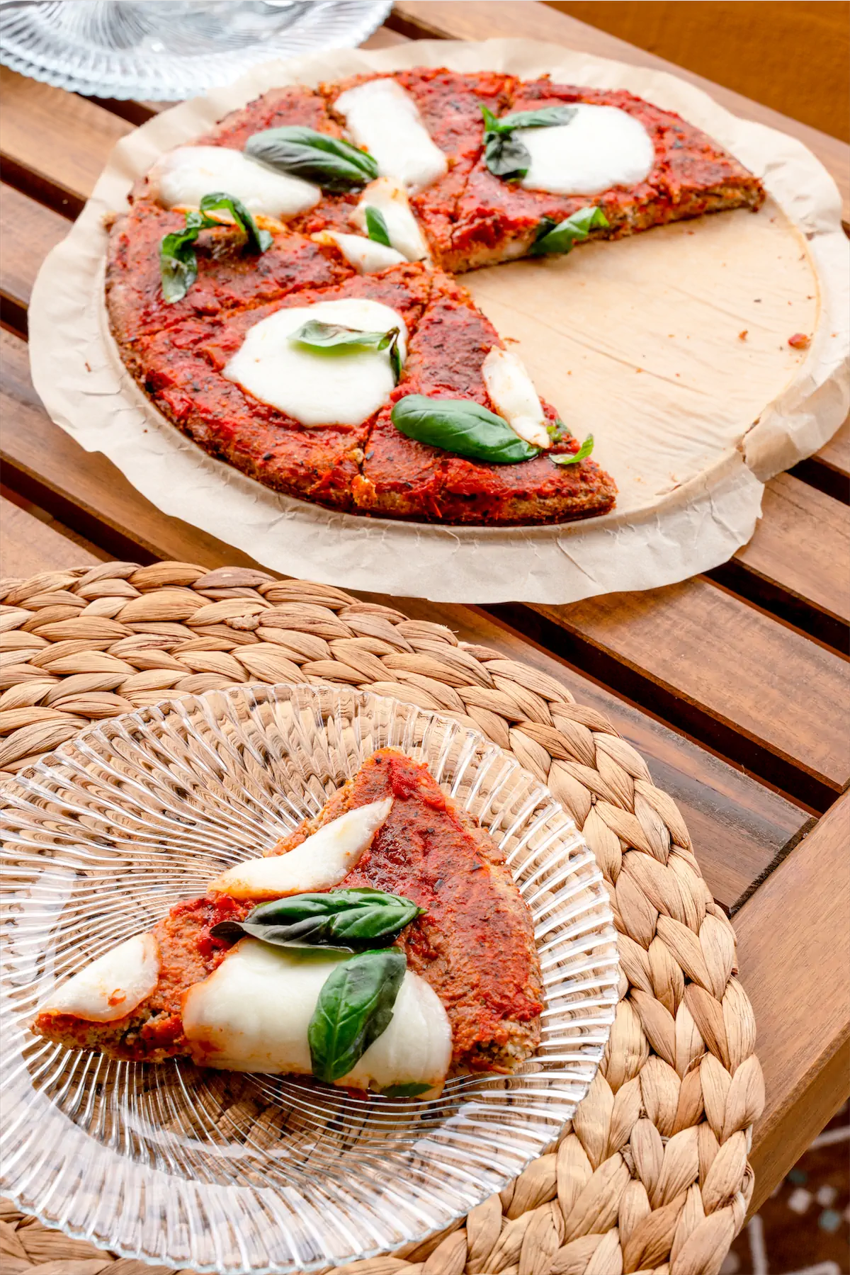 A slice of pizza served in a glass plate next to rest of the pizza on a wooden pizza board.