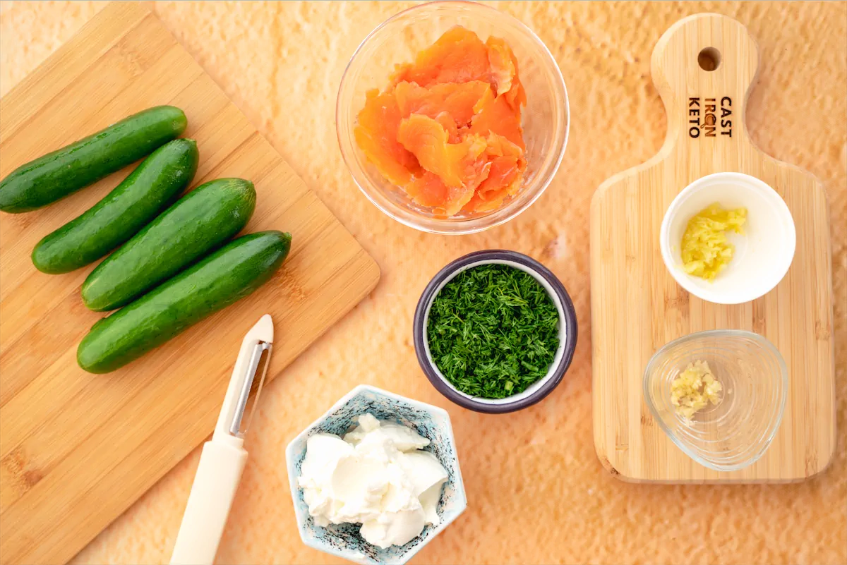 Cucumbers, smoked salmon, minced garlic, fresh dill, ginger, and other preparation items placed on the kitchen table.