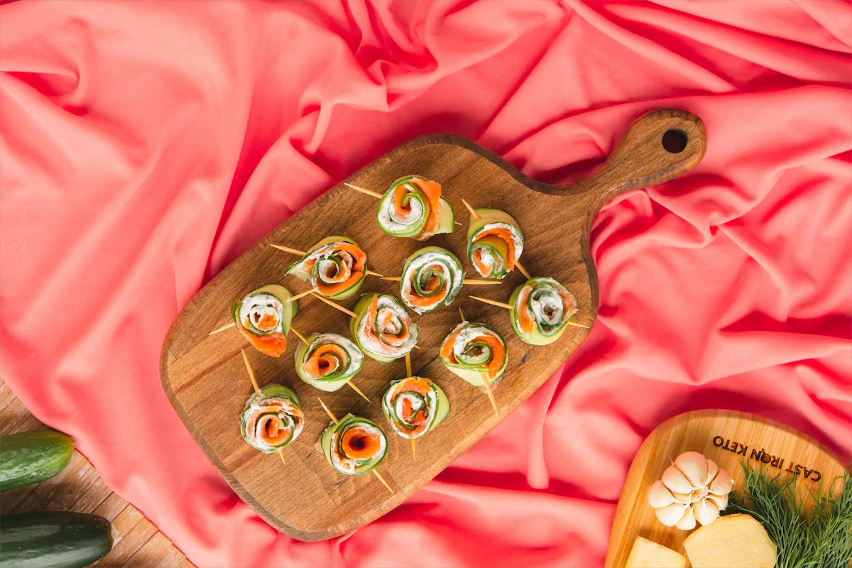 Keto salmon cucumber rolls on wooden serving tray on kitchen table.