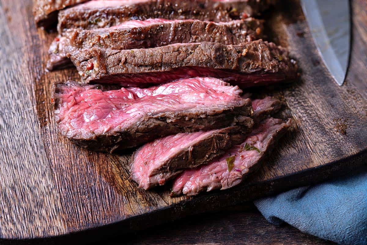 close up of a sliced grilled skirt steak on a wooden cutting board.