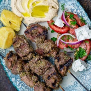 Lamb kabobs served on a plate with a tomato salad and hummus