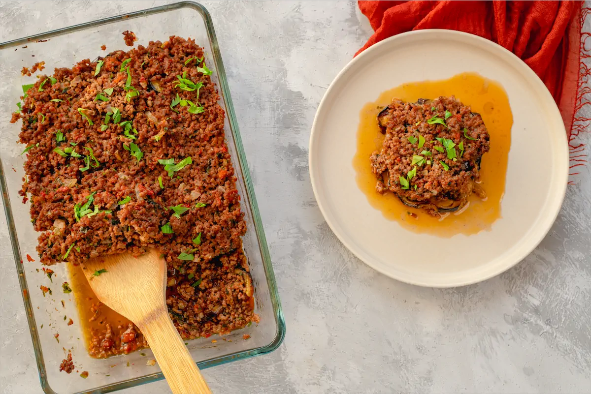 Keto moussaka recipe served on a plate from glass baking dish with wooden spatula.