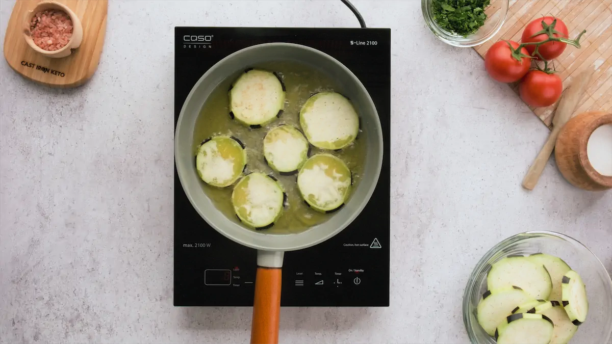 Sliced eggplants getting fried in hot oil in a pan.