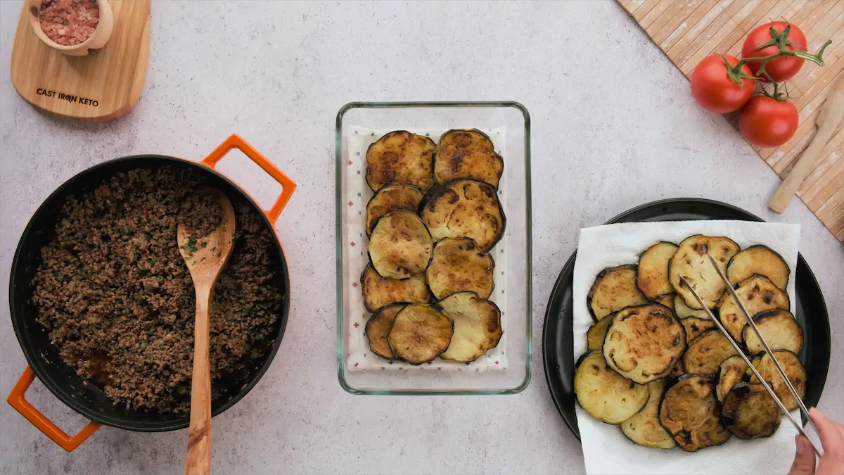 Cooked grown beef in a skillet and sliced fried eggplants.