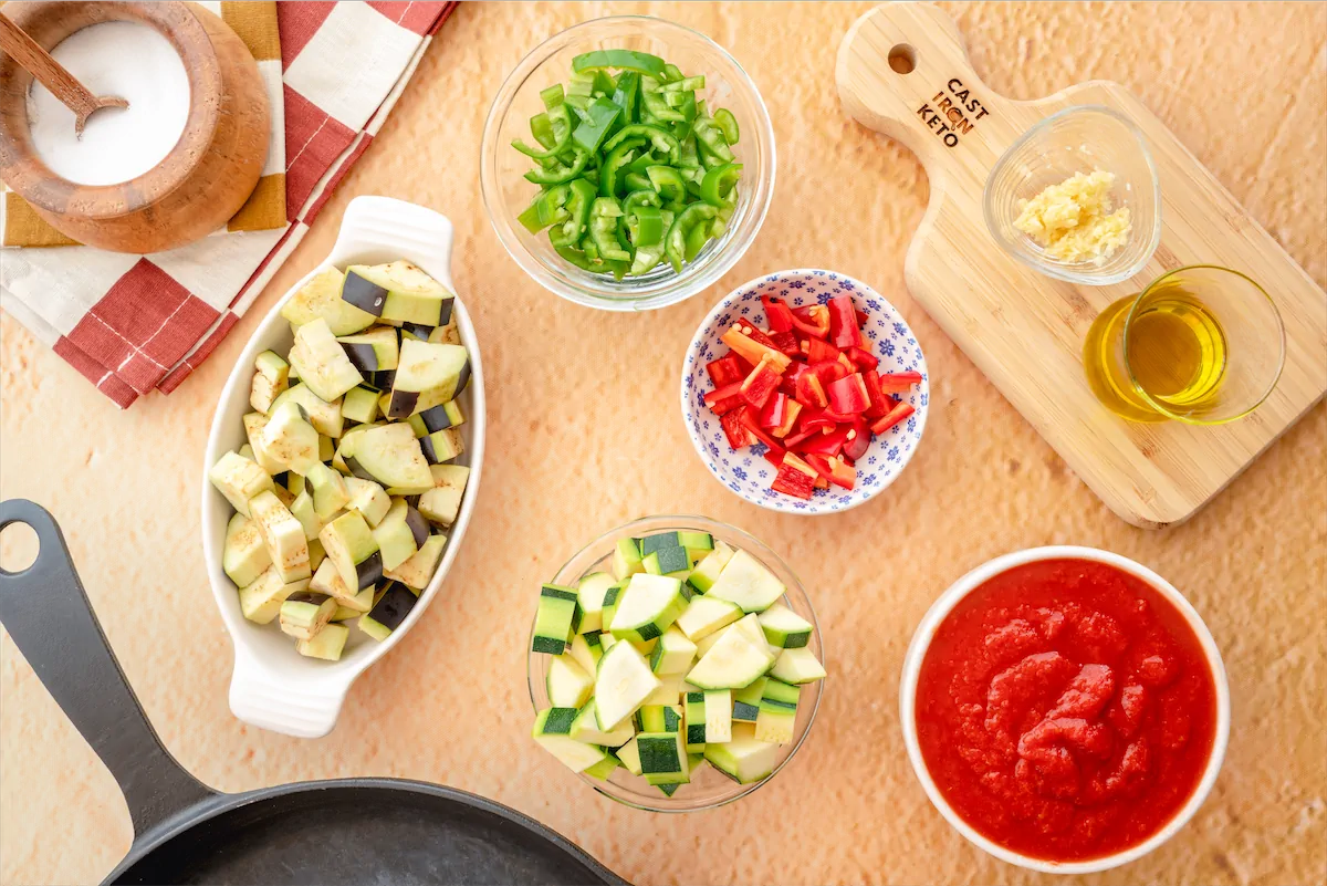 Chopped eggplant, zucchini, bell peppers, garlic, canned chopped tomatoes, oil, salt, black pepper, and, apple cider vinegar made ready on the kitchen table.