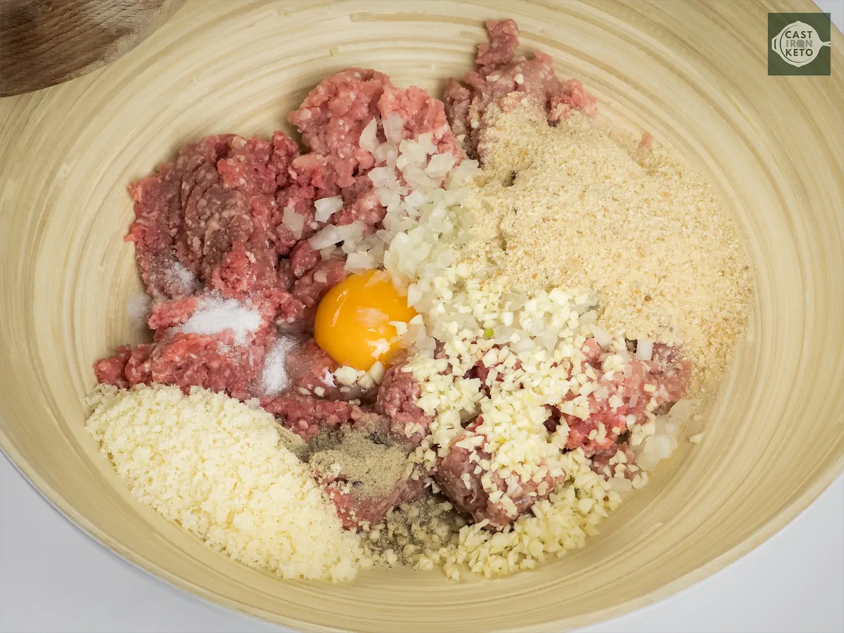 Ground beef, ground pork, egg, finely chopped onion, minced garlic, finely grated parmesan cheese, keto bread crumbs, salt, and pepper mixed in a large bowl.