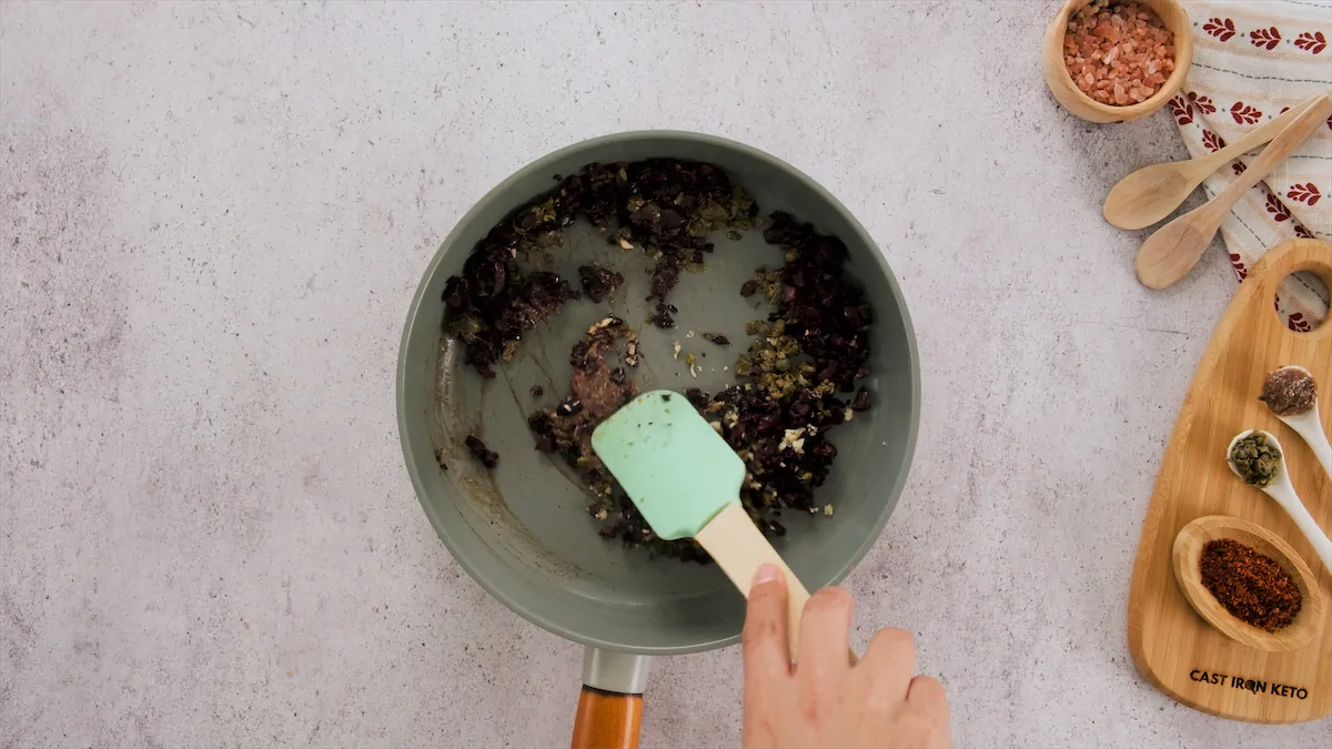 Sautéing ingredients like minced garlic, capers, and anchovy fillets in a skillet.