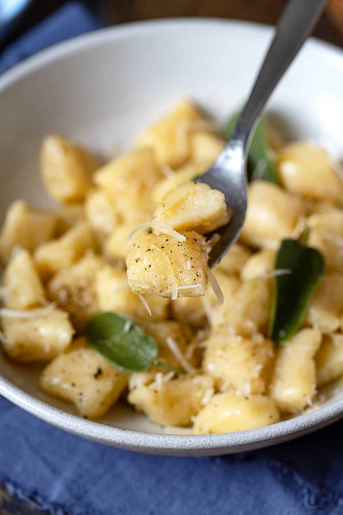 close up of a bite of ricotta gnocchi being lifted from a bowl with a fork.