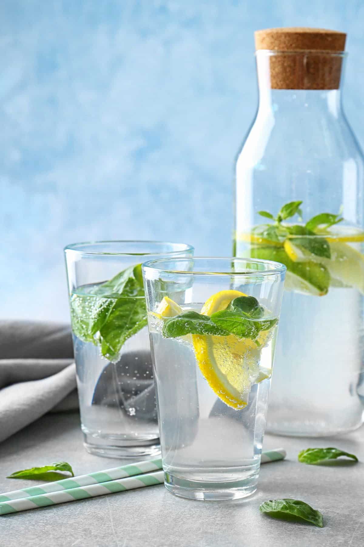 A pitcher of basil water with two glasses and lemon wedges.