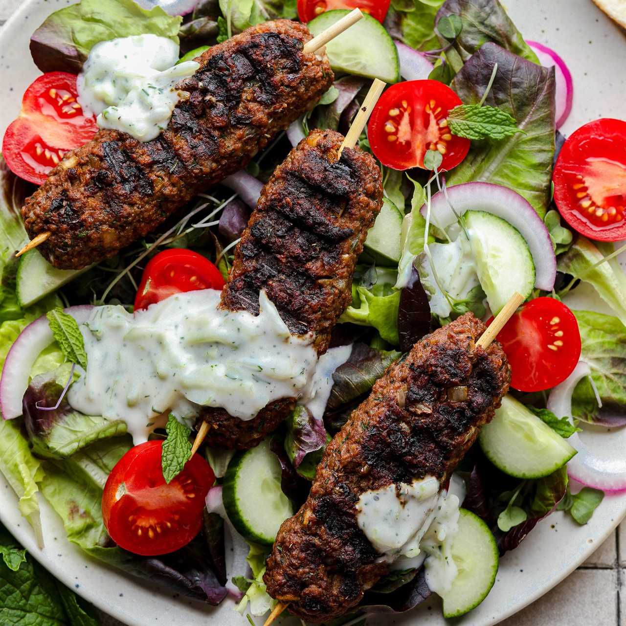 grilled vegan kofta on top of a green salad with vegetables and tzatziki.