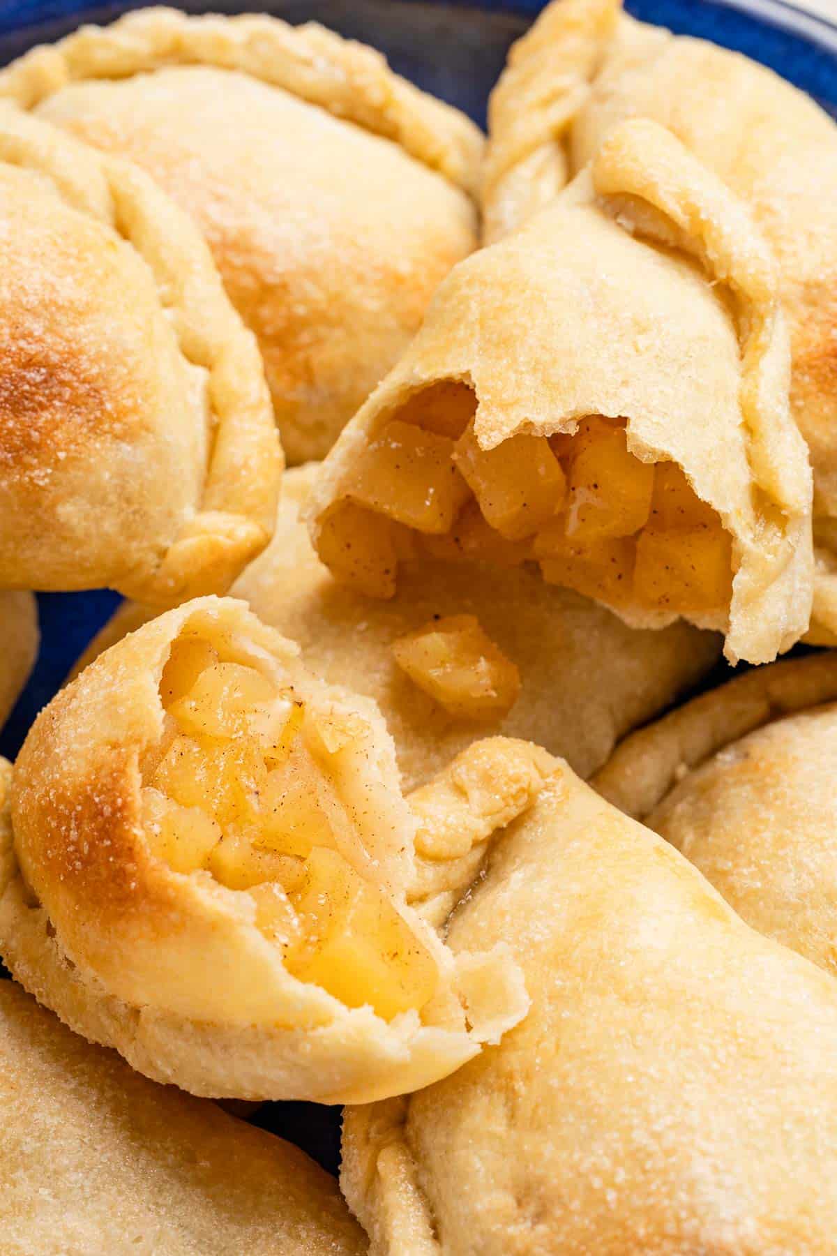 a close up of a baked apple empanada cut in half on a stack of other apple empanadas.