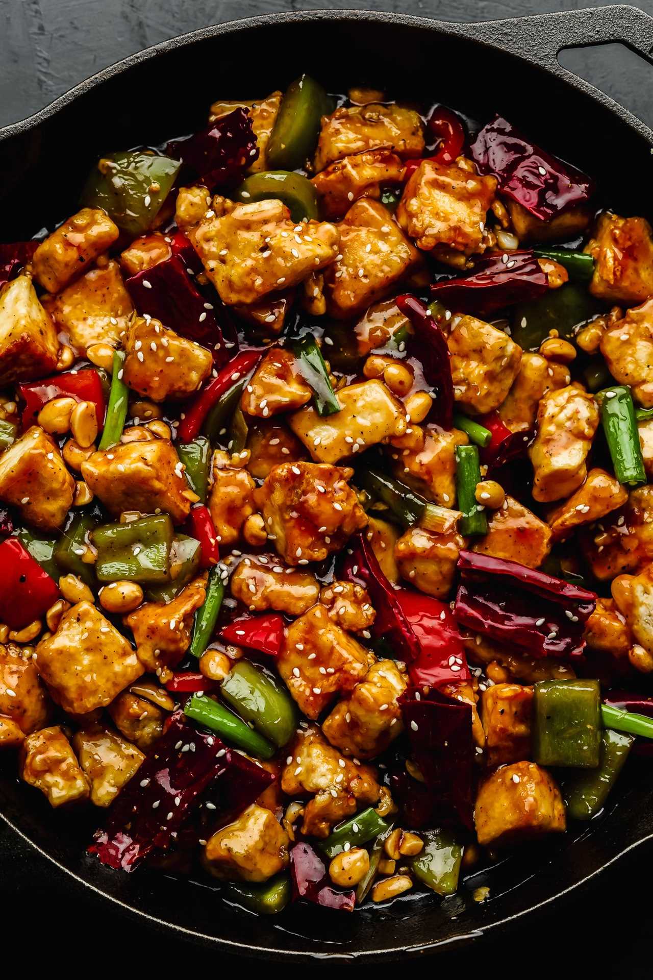 close up on cooked kung pao tofu and vegetables in a large black cast iron skillet.