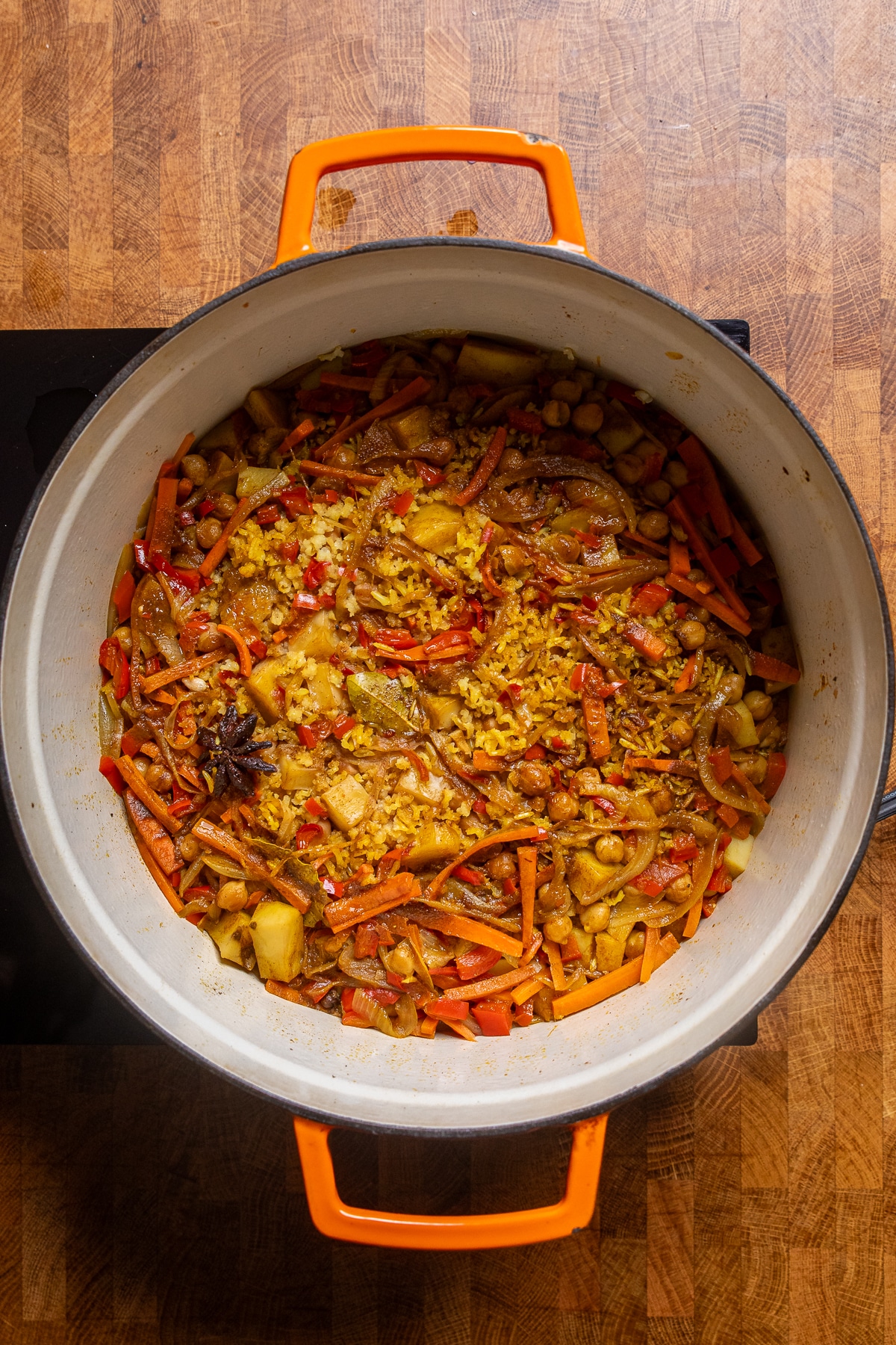 cooking vegetable biryani in a large white and orange dutch oven.