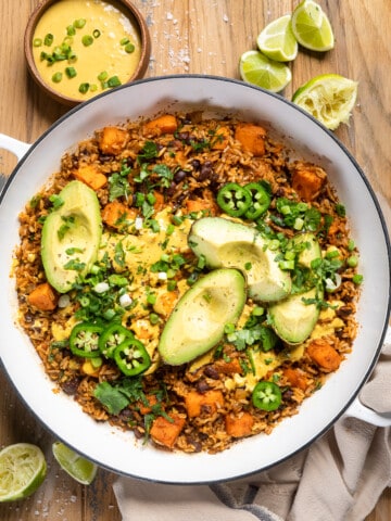 vegan southwest rice in a large white skillet with avocado wedges on top.