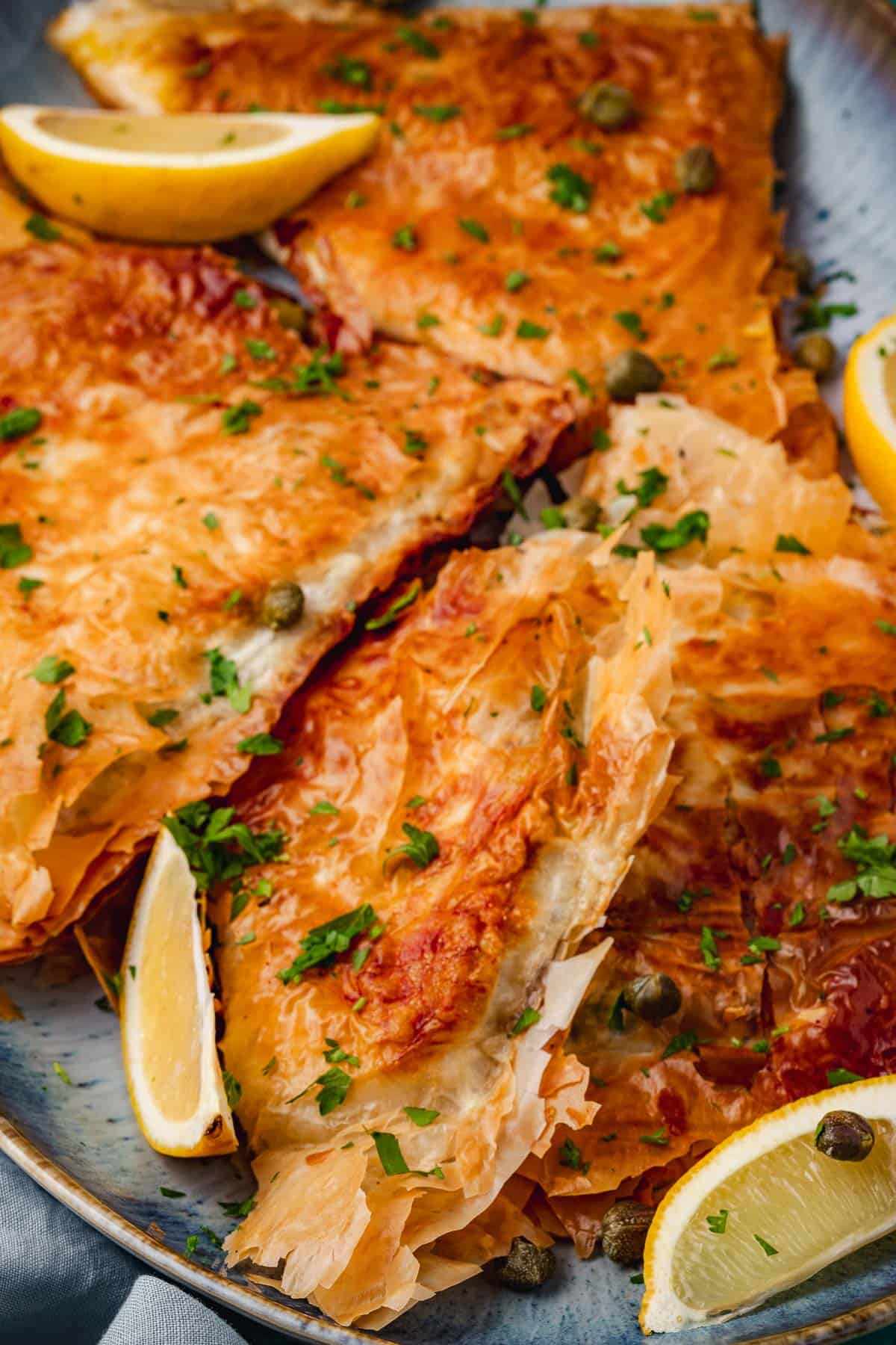 a close up of pieces of brik on a serving platter with lemon wedges.