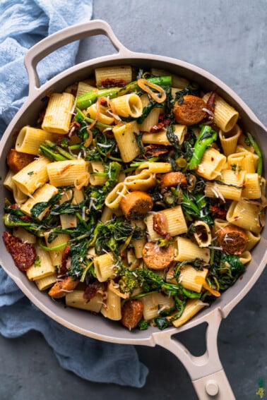 an overhead photo of the Vegan Broccoli Rabe & Sausage Pasta in a pot with blue towel on a grey background.