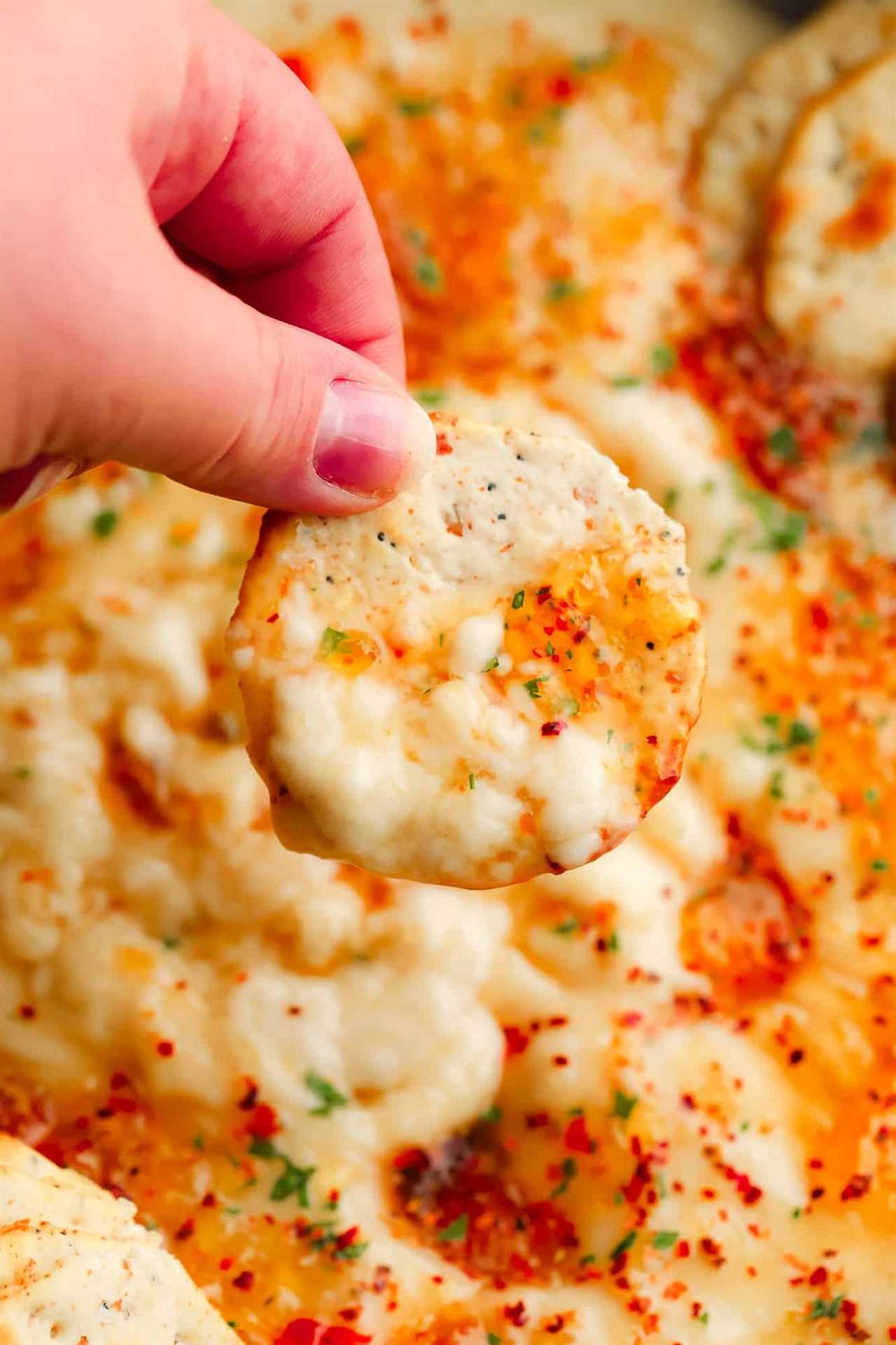 womans hand holding a cracker dipped in vegan brie with pepper jelly.