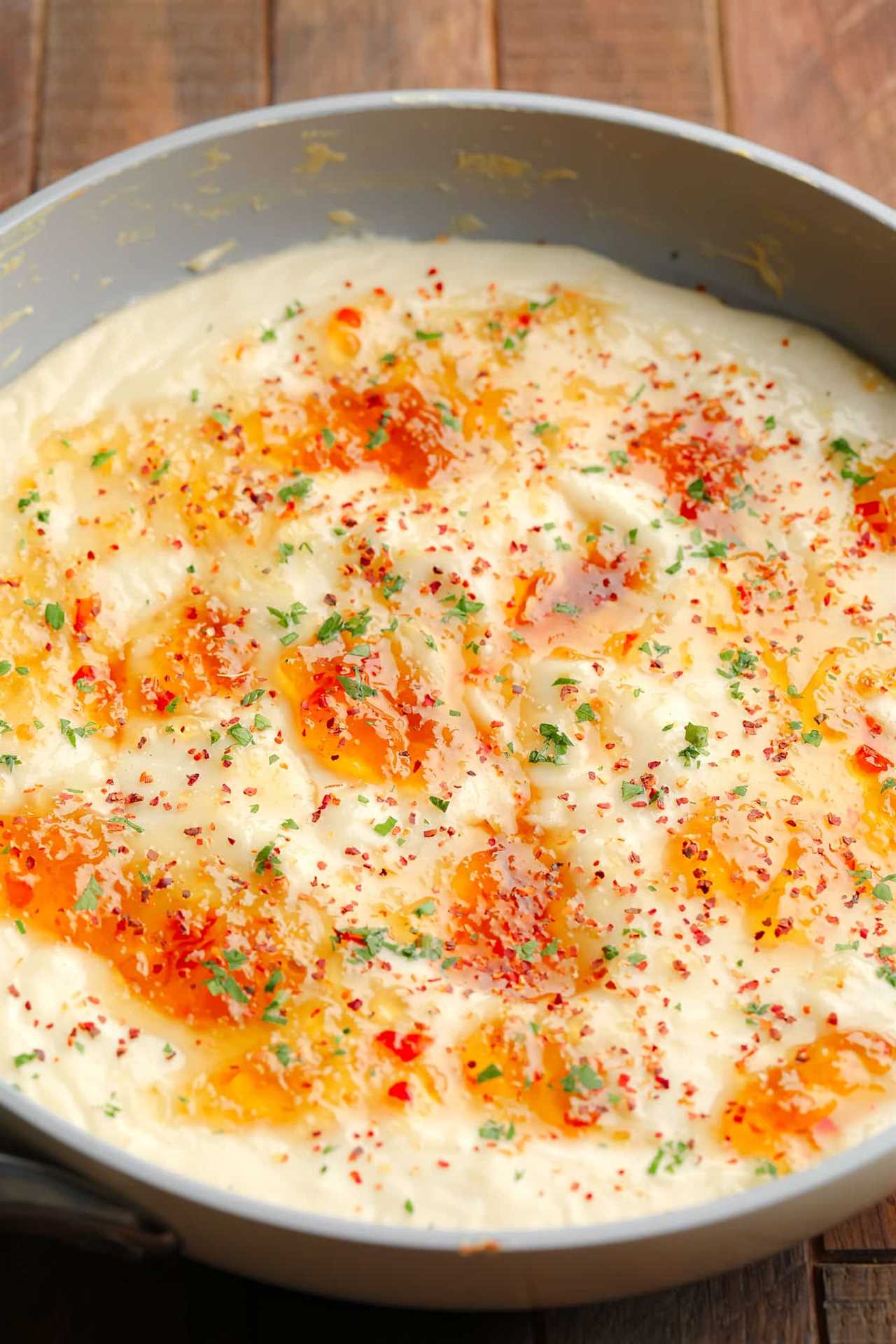 baked vegan brie dip topped with pepper jelly in a grey saucepan.