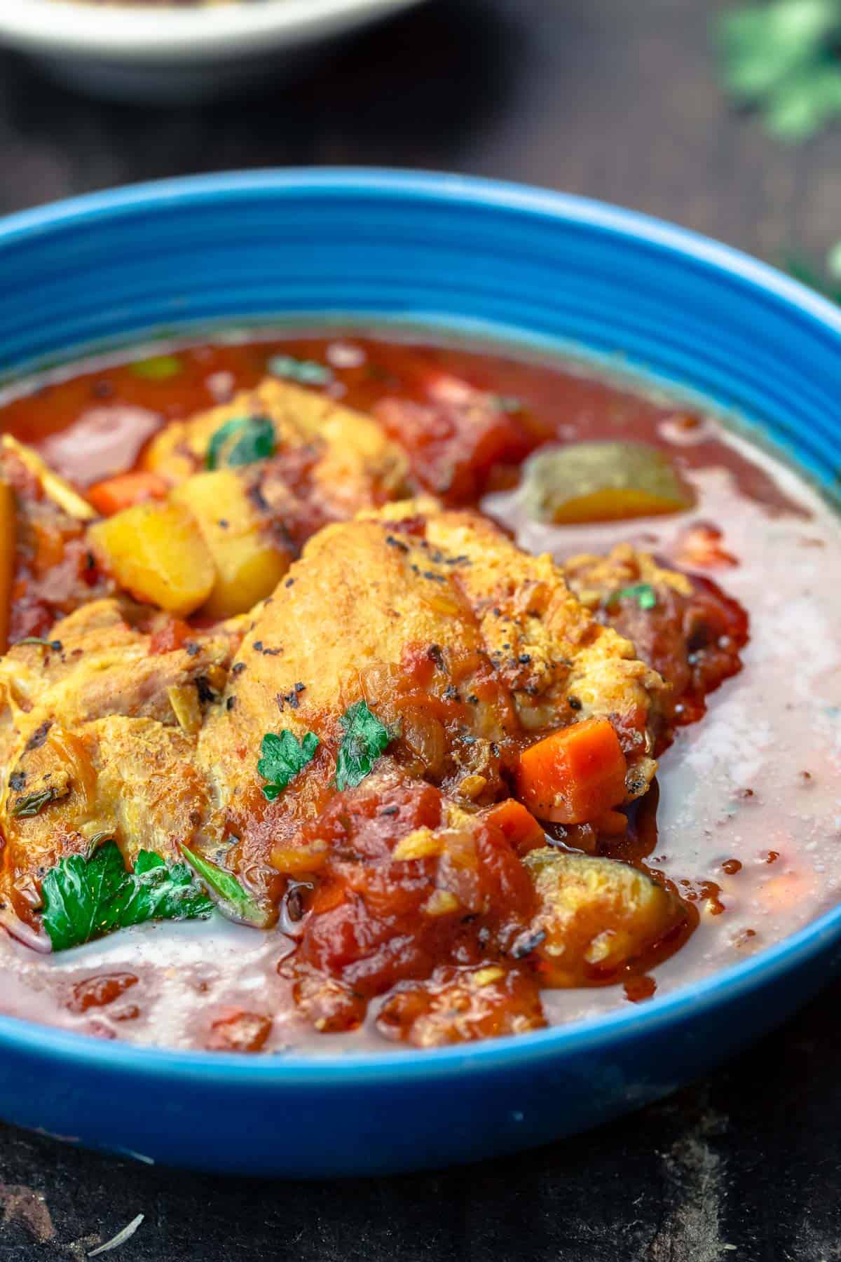 a serving of chicken stew garnished with parsley in a blue bowl.