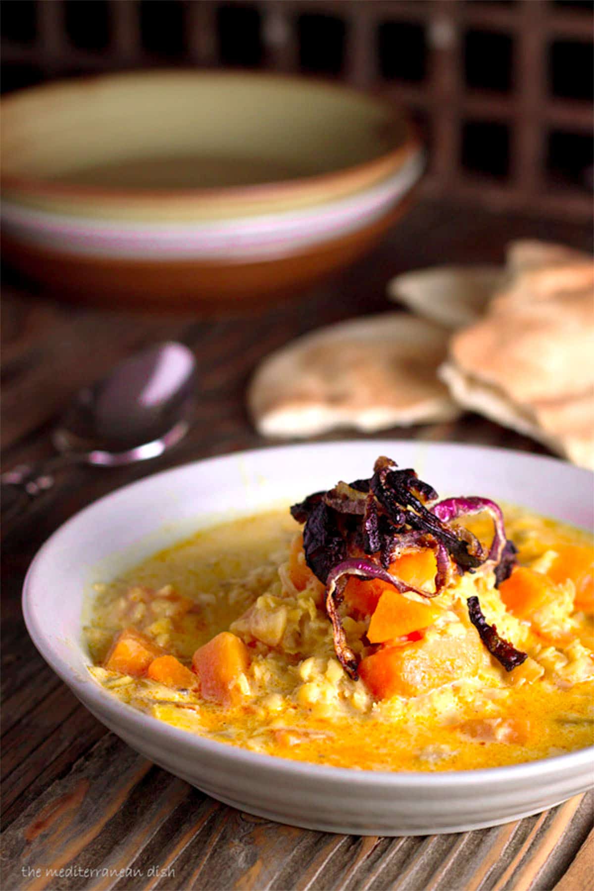 curried red lentil soup in a bowl with pita bread in the background.