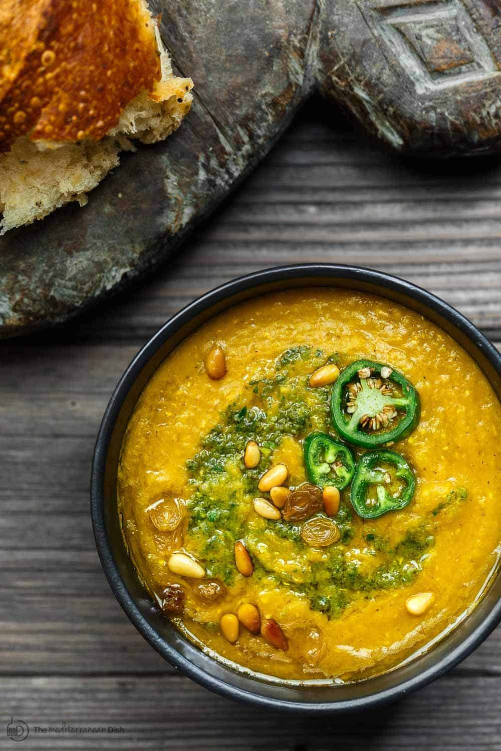 Bowl of pumpkin soup topped with jalapeno with a side of crusty bread