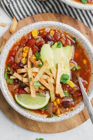 A bowl of vegan tortilla soup with garnishes and a spoon