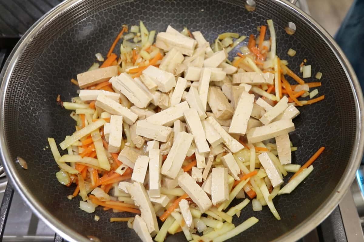 step by step - tofu being added to sweet potato, carrot, garlic and onion