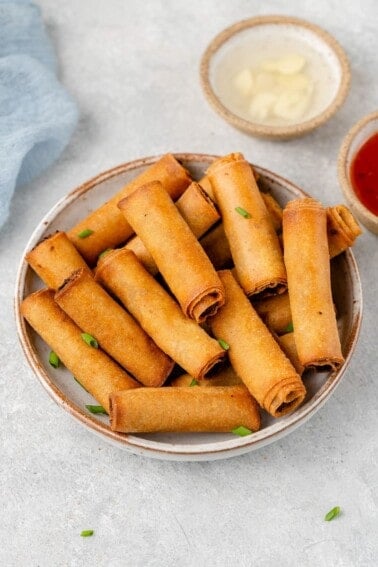 shot of Filipino Lumiang Shanghai in a white bowl with dipping sauces by sweet simple vegan