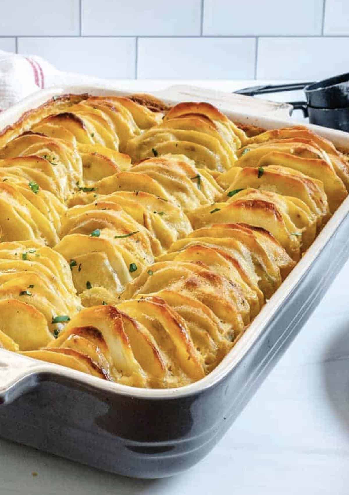 Casserole dish with baked vegan scalloped potatoes topped with chives.