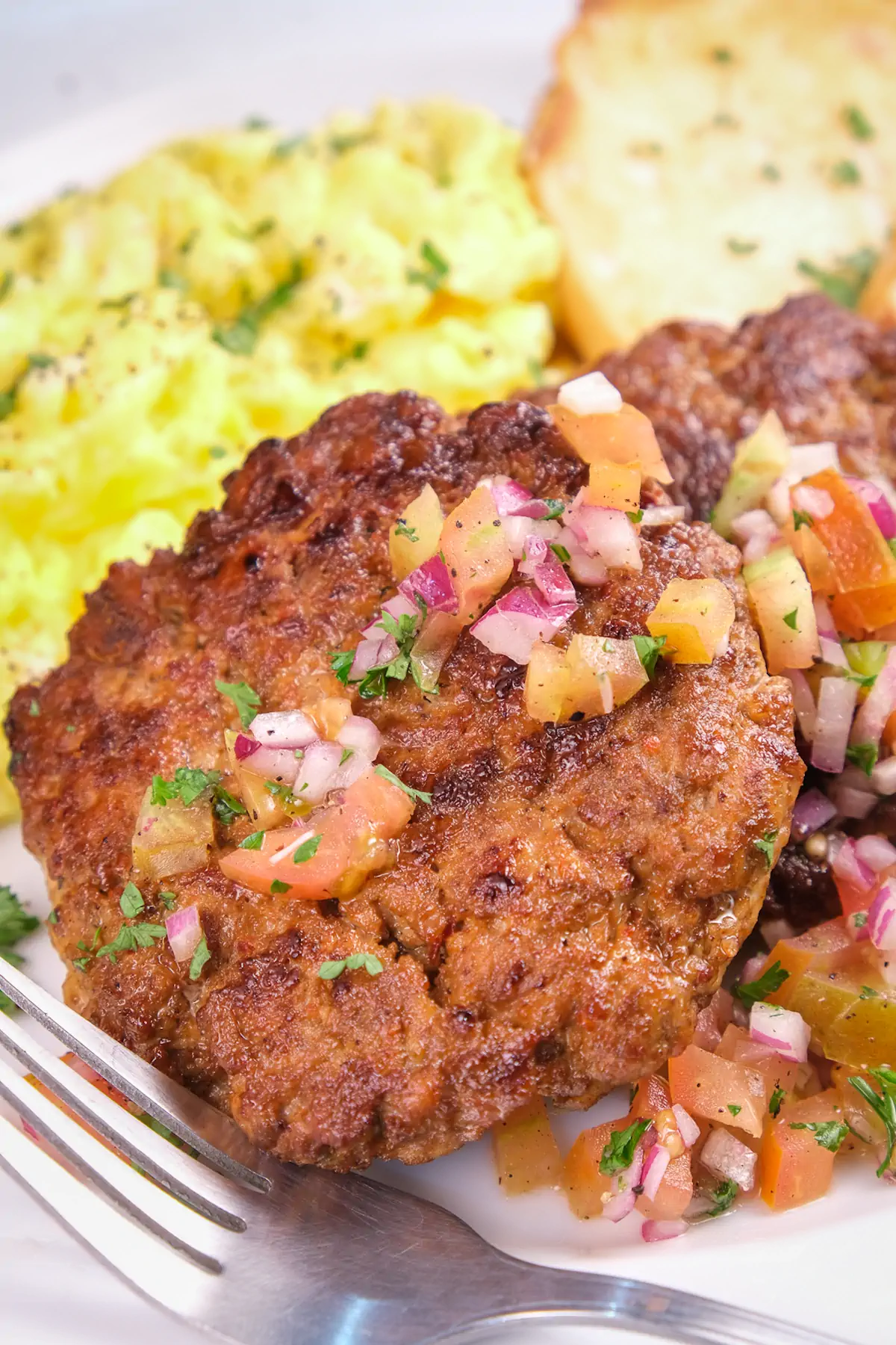 A focused shot of keto breakfast sausage topped with diced tomatoes and onions.