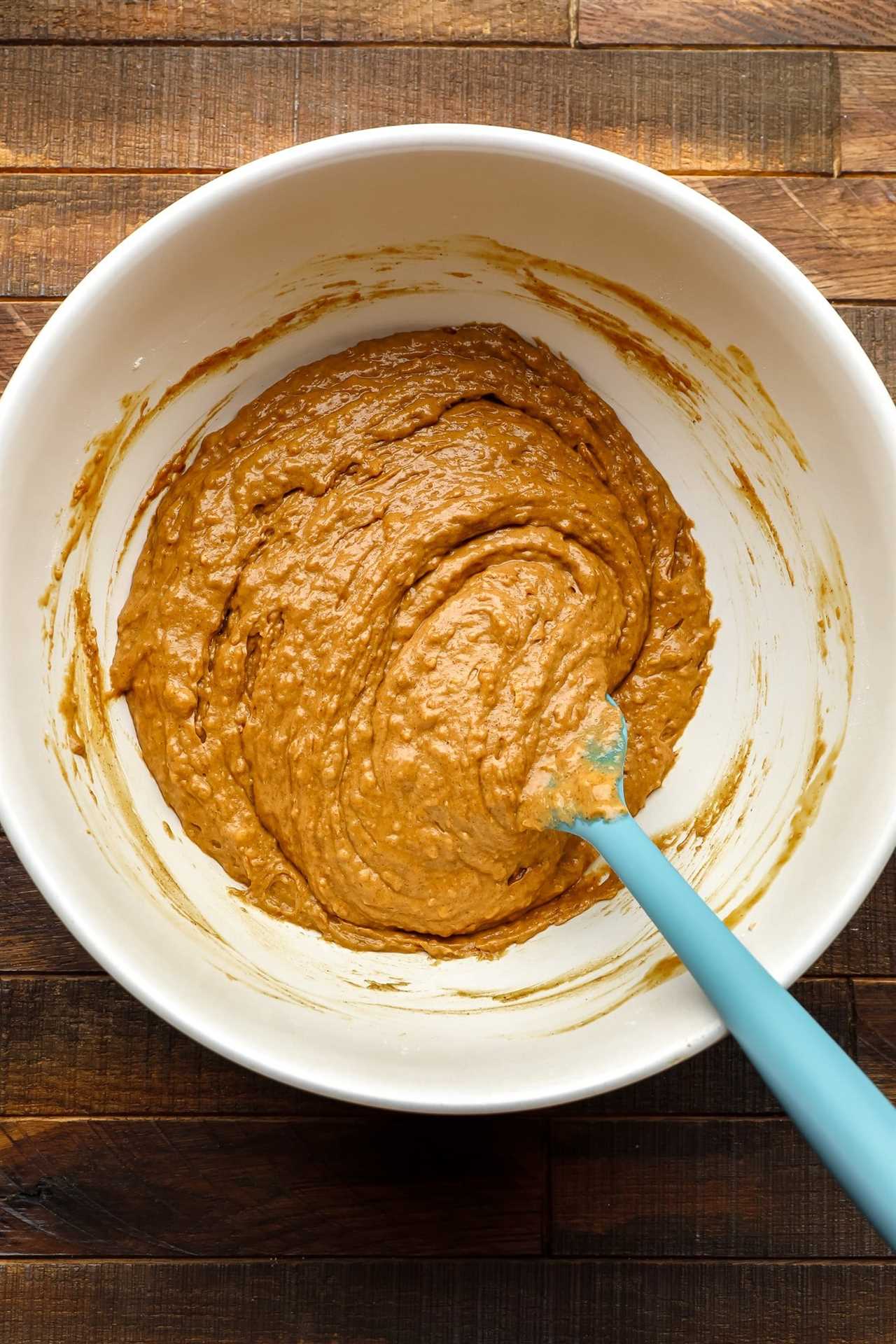 using a spatula to stir batter for a gingerbread loaf in a large white bowl.