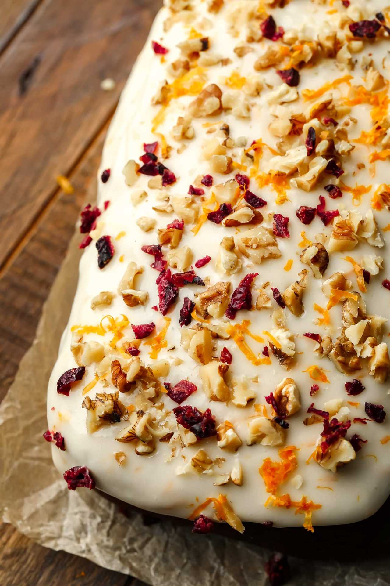 close up on cream cheese icing decorated with nuts, dried cranberries, and orange zest on a gingerbread loaf.
