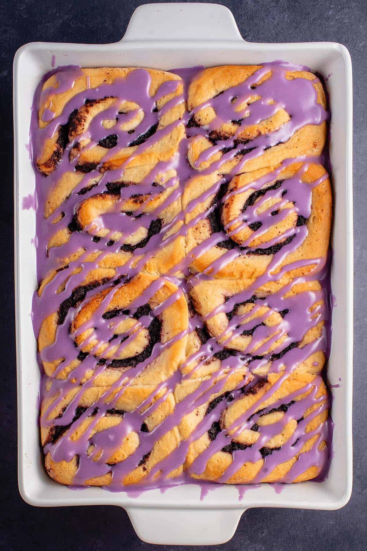 baked ube cinnamon rolls with purple icing in white dish