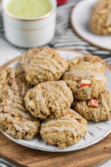 close up of apple cinnamon oatmeal cookies on white plate next to matcha latte