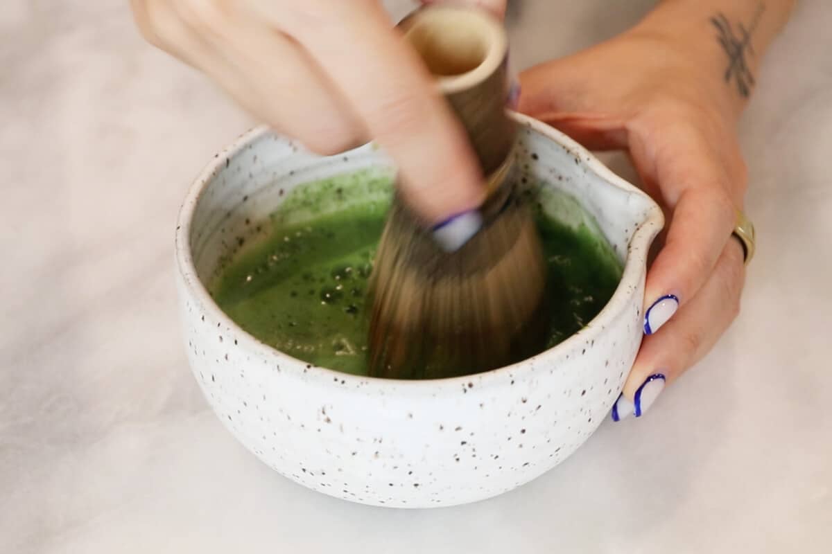 whisking matcha in white bowl with chasen