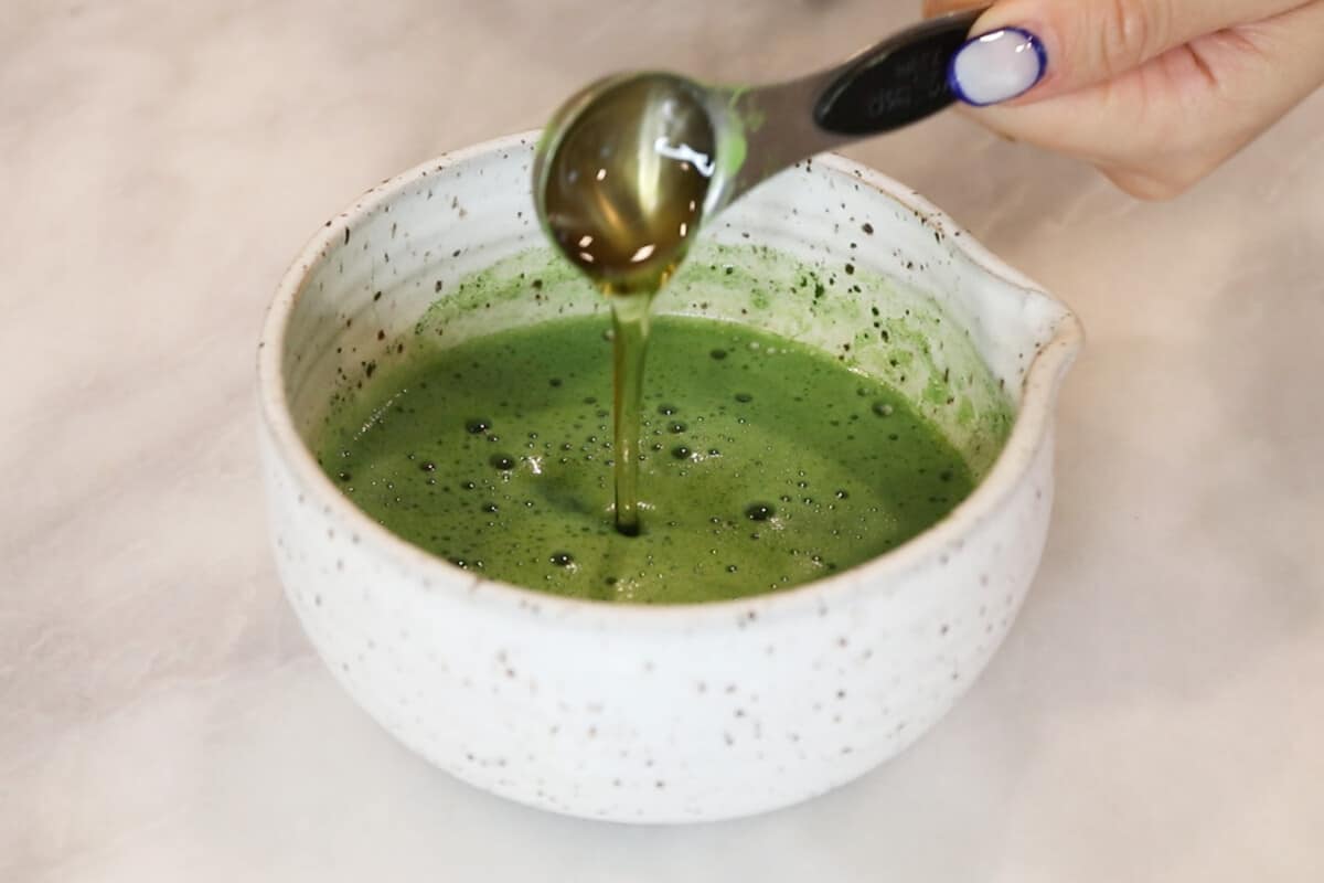 adding sweetener to matcha in white bowl