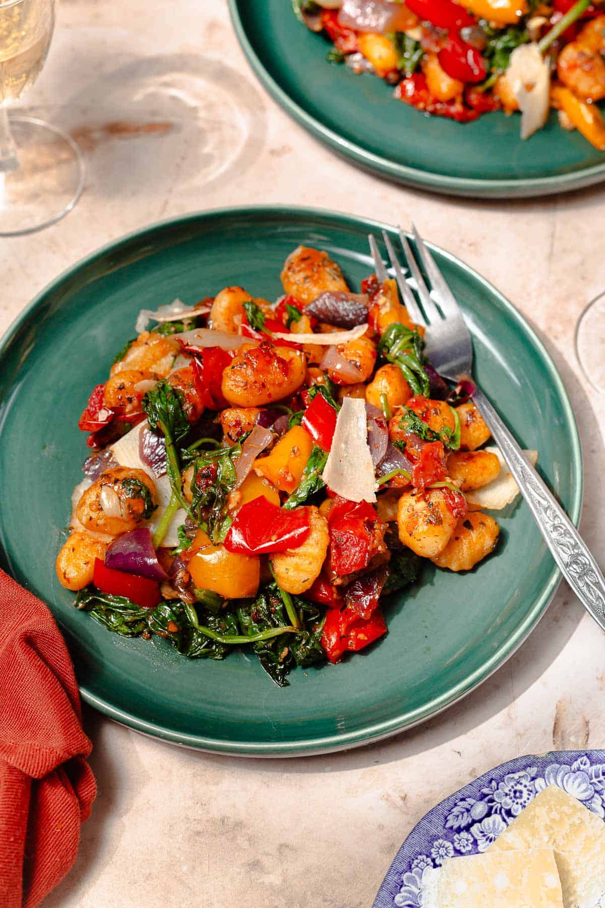 a serving of sheet pan gnocchi on a teal plate with a silver fork and white wine on the side.