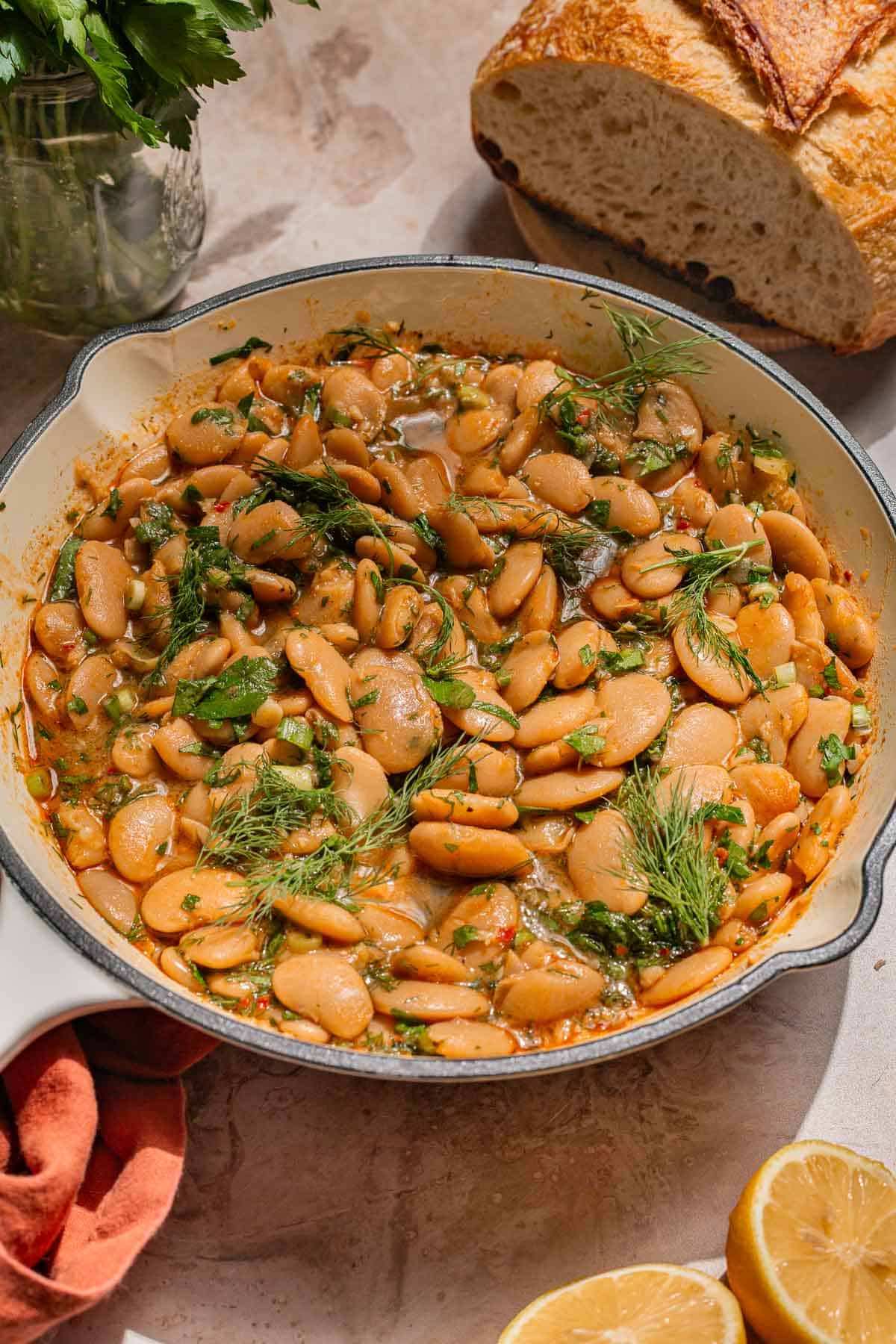 Side shot of butter beans in a white pan with bread and lemon wedges on the side.