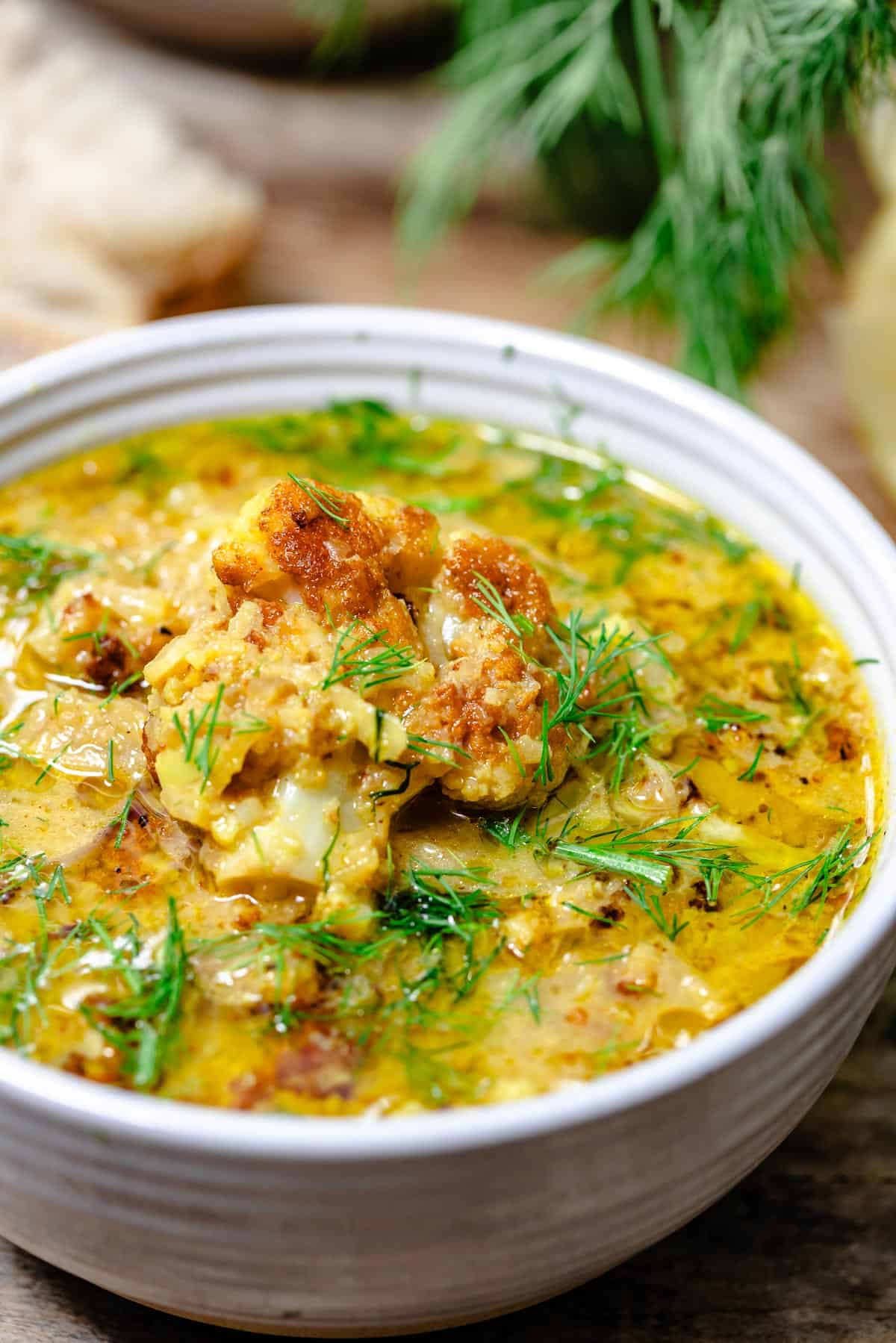 a close up of roasted cauliflower soup in a bowl garnished with dill.