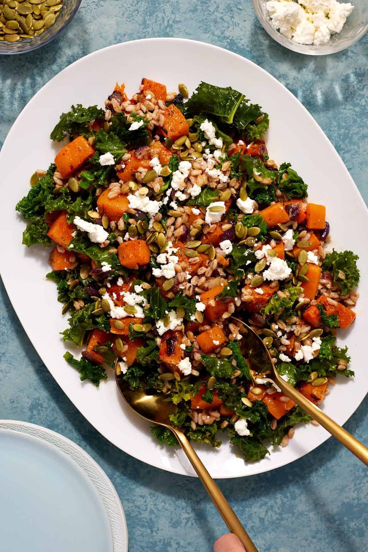 butternut squash salad on a serving platter with gold serving utensils.